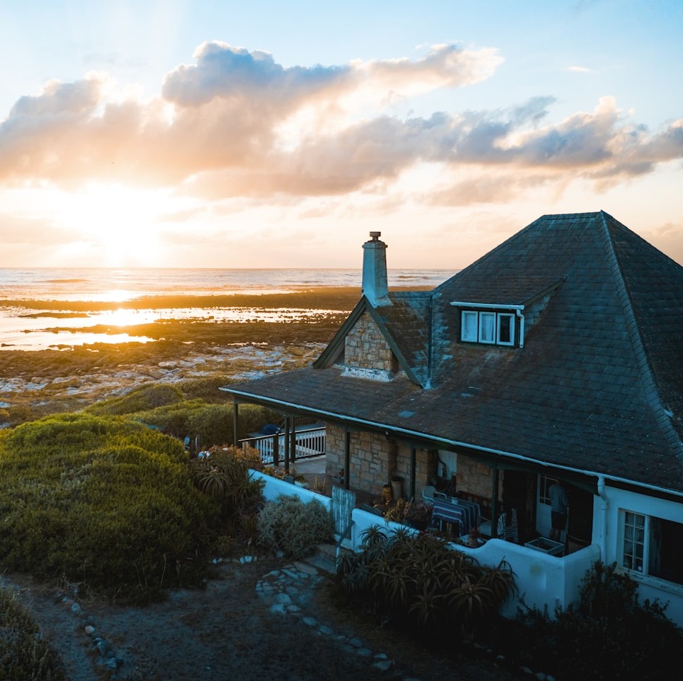 Stone cottage with a steep dark roof on a rocky coastal hillside overlooking the sea at golden hour